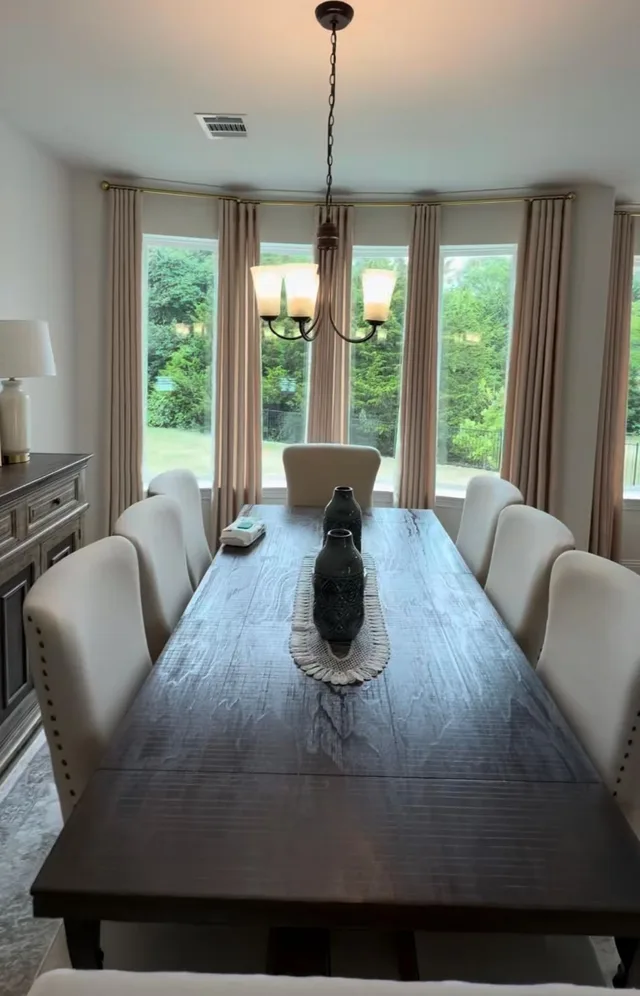 Beige curtain panels on a gold-toned rod around bay windows in a dining room.