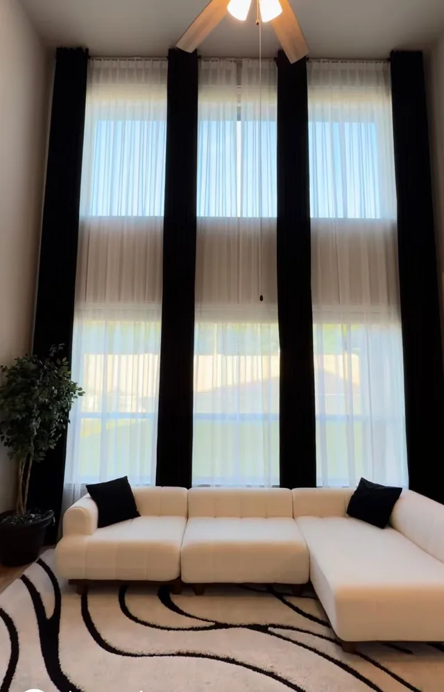 Black curtain panels and white sheers across tall windows behind a white sectional.