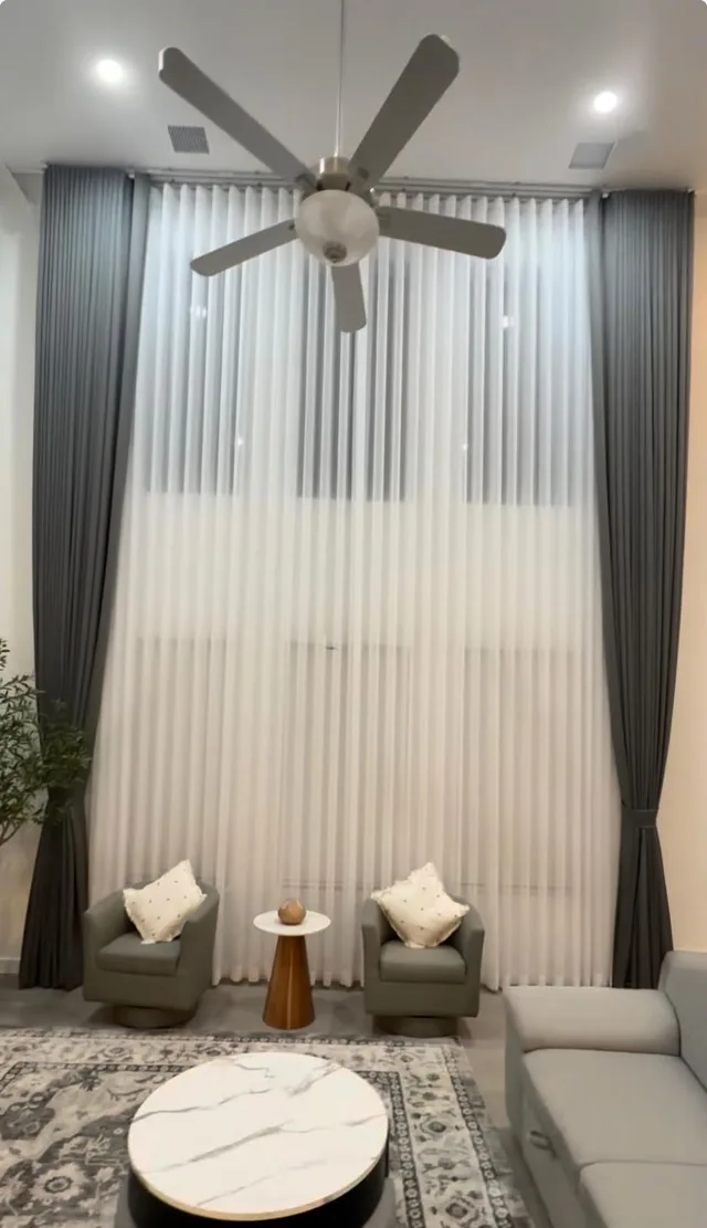 Charcoal side drapes and white sheers spanning double-height windows behind two armchairs.