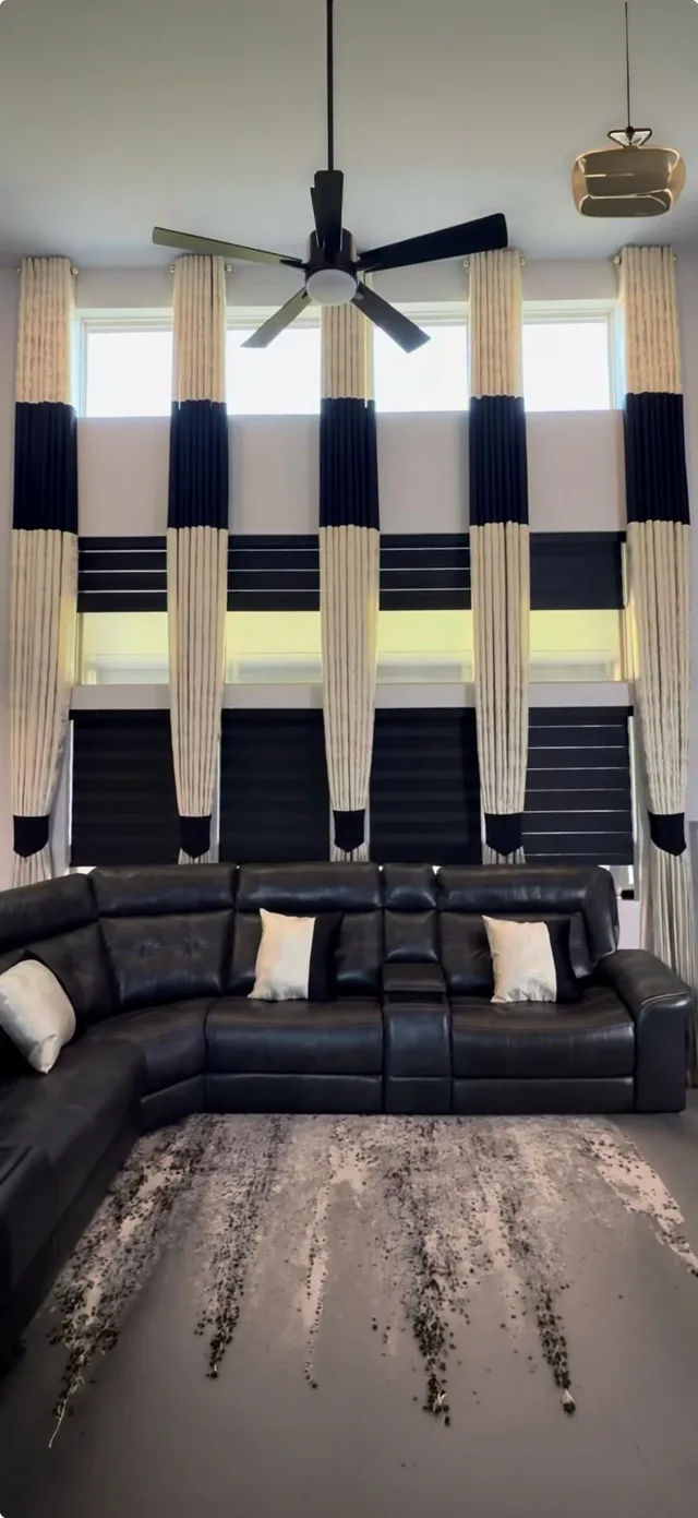 Cream curtains with navy accent bands and dark zebra blinds behind a black sectional.