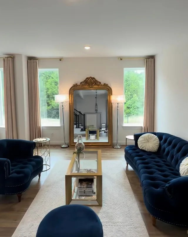 Neutral curtain panels framing narrow windows beside a gold mirror and blue seating.
