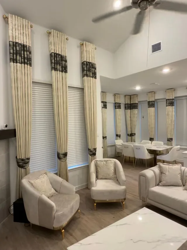 Cream patterned drapes with dark accent bands and white blinds in connected living and dining spaces.