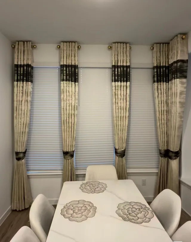 Cream patterned curtain panels with dark bands and tiebacks over white dining room blinds.