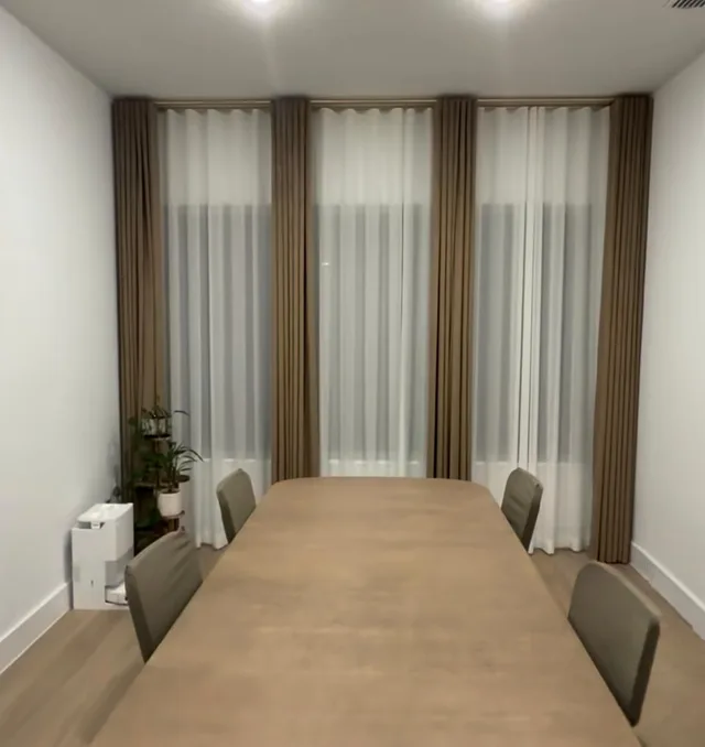 Taupe curtain panels and white sheers behind a long wooden dining table.