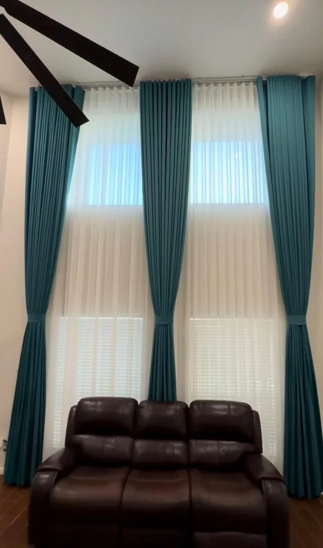 Tall teal drapes tied back over white sheers in a double-height living room.